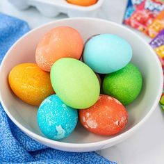 a white bowl filled with colored eggs on top of a blue and white table cloth