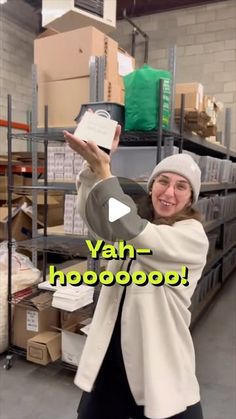 a woman is holding up a sign in the middle of a room with shelves and boxes