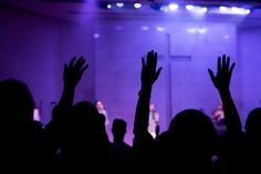 silhouettes of people raising their hands in front of a stage with purple lighting and lights