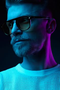 a man with sunglasses on his face looking at the camera while standing in front of a dark background