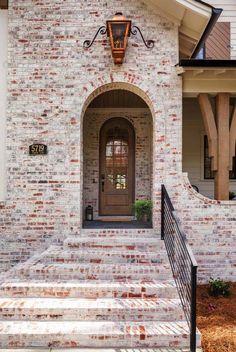 a brick house with a wooden door and black iron railing on the front porch area