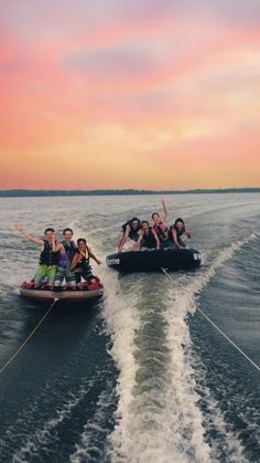 several people on jet skis being pulled by a boat in the water at sunset