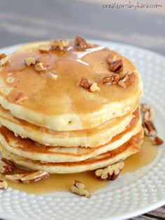 a stack of pancakes covered in syrup and pecans on a plate with maple syrup drizzled over the top