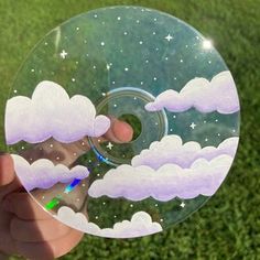 a hand holding a glass plate with clouds and stars in the sky on top of it