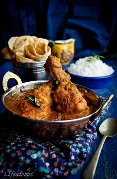 some food is sitting in a bowl on a blue tablecloth with silver spoons