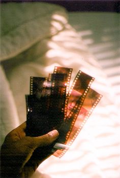 a hand holding four film strips in front of a white sheet with shadows on it