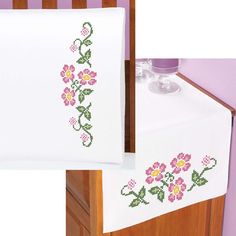 a cross - stitch table runner with flowers on it and a bottle holder in the corner