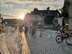 several people riding bicycles on a cobblestone road at sunset in the middle of town