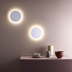 two round lights are on the wall above a bowl and cup in front of it