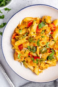 a white bowl filled with pasta and vegetables on top of a table next to silverware