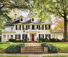 a large white house with black shutters on the front and side windows, surrounded by trees