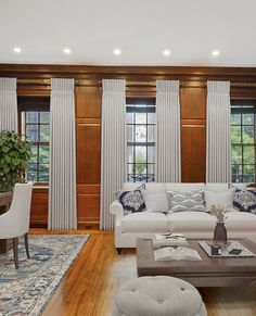 a living room with wood paneling and white couches in front of two windows