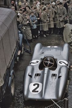 an old race car is parked in front of a crowd