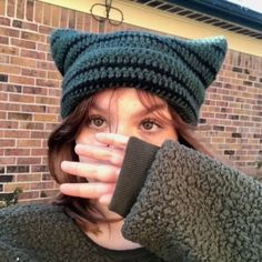 a woman wearing a green hat covering her face with one hand and looking at the camera