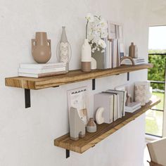 two wooden shelves with books, vases and other items on them against a white wall