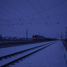 a train traveling down tracks next to snow covered ground and power lines in the background