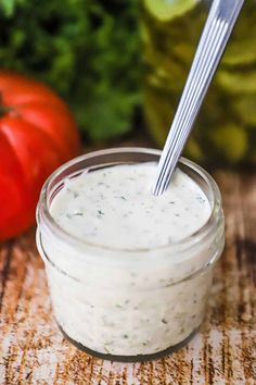 a jar filled with dressing sitting on top of a table next to tomatoes and lettuce