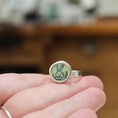 This adorable Rabbit ring has a vintage storybook quality.Available in whole sizes 6 through 9I carved the sterling silver setting from a block of wax, then cast that wax pendant into metal and molded it so I can make multiples. Both sides of the setting then get a layer of vitreous enamel (fine glass) and fired at 1400 degrees in a kiln, four separate times, to build strength and color saturation . Finally I take an illustration from my sketchbook, turn it into an enamel screen print, and fire Rabbit Ring, Vintage Storybook, Vitreous Enamel, Build Strength, Dog Jewelry, Enamel Necklaces, Enamel Bracelet, Enamel Ring, Cat Necklace