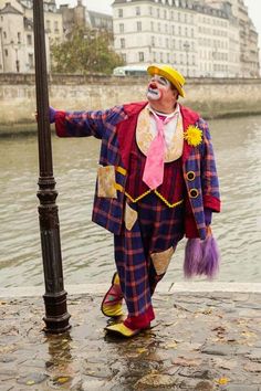 a man dressed as a clown standing next to a lamp post