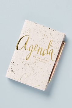 an agenda book with gold foil lettering on it and a pen laying next to it