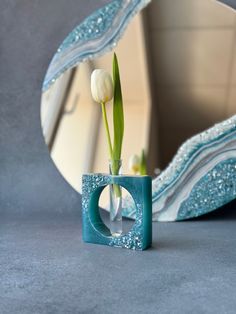 a vase with a flower in it sitting next to a mirror and a decorative object