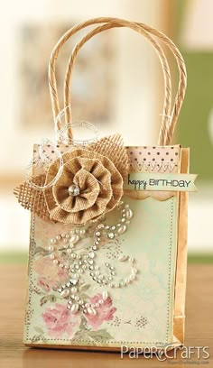 a small gift bag with a flower on the front and ribbon around it's handle