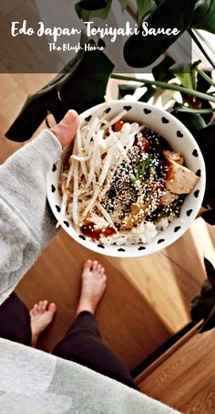 a person holding a bowl of food on top of a wooden table next to a potted plant