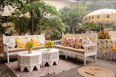 an outdoor seating area with yellow and white pillows on the couches, tables and umbrellas