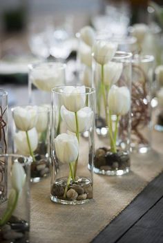 there are many vases with white flowers in them on the table cloth, along with rocks and pebbles