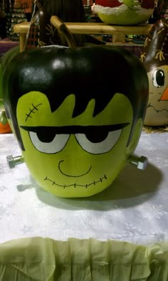 a large green pumpkin with eyes and mouth painted on it's side sitting on a table