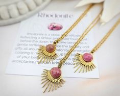 Bring celestial beauty to your look with our Rhodonite Gemstone Sunburst Necklace. It features your choice of 14-inch, 18-inch, or 22-inch stainless steel chain, and holds a stunning sunburst pendant with a beautiful polished natural rhodonite gemstone. This is a simplistically stunning design that is must-have. Each necklace comes with a coordinating affirmation card, with gemstone meaning on one side, and a positive affirmation on the other side.  NECKLACE LENGTH: You may select between 14-inch, 18-inch, and 22-inch chains PENDANT SIZE: 20.5mm x 26mm MATERIAL: Stainless Steel, Natural Rhodonite Gemstone COLOR: You may select between gold and silver at checkout QUANTITY: 1 Necklace For more WONDERLIGHT designs, CLICK HERE! https://www.etsy.com/shop/SpotLightJewelry?ref=seller-platform-mcn Rhodonite Jewelry, Sunburst Necklace, Sugar Skull Earrings, Gold Sunburst, Gemstone Meanings, Celestial Necklace, Girl Jewelry, Gold Necklace Designs, Silver Jewelry Pendant