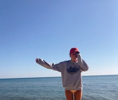 a woman standing on top of a beach next to the ocean with her arms outstretched