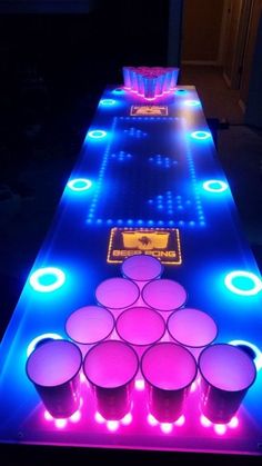 an illuminated table with cups on it and neon lights at the top, along with plastic cups lined up in rows