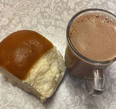 a cup of coffee next to a piece of bread on a tablecloth covered table