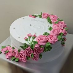 a white cake decorated with pink roses and green leaves