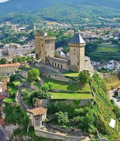 an old castle on top of a hill in the middle of town with trees and buildings around it