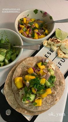 a table topped with two tortillas covered in veggies next to a bowl of salad