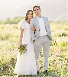 a bride and groom posing for a photo in a field with mountains in the background