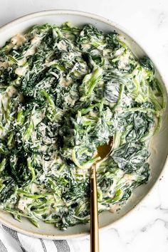 a white bowl filled with spinach and cheese on top of a marble countertop