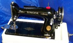 an antique singer sewing machine sitting on top of a blue cloth covered table next to a red button