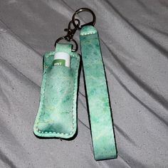 a green leather keychain with an empty bottle in the center and a white tube on it