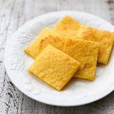 four pieces of cheese crackers on a white plate sitting on a wooden table top