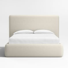 an upholstered bed with white sheets and pillows