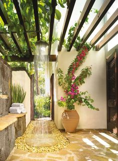 an outdoor shower with flowers and greenery on the wall, next to a stone bench