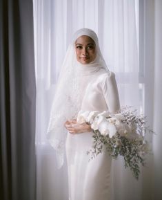 a woman wearing a veil and holding a bouquet of flowers in front of a window