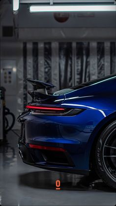 the back end of a blue porsche sports car in a garage with its hood open