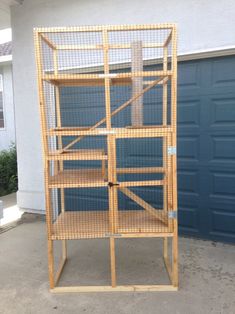 a tall wooden bird cage sitting in front of a garage