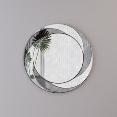 a round mirror with a palm tree in the middle on a gray wall behind it