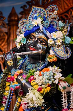 an idol is dressed in blue and white with flowers on his head, holding a flute