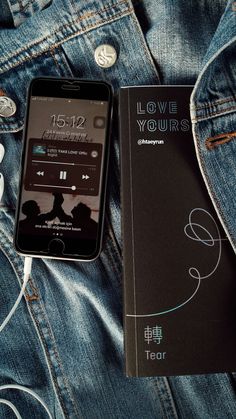 an mp3 player sitting on top of a pair of jeans next to a book and headphones